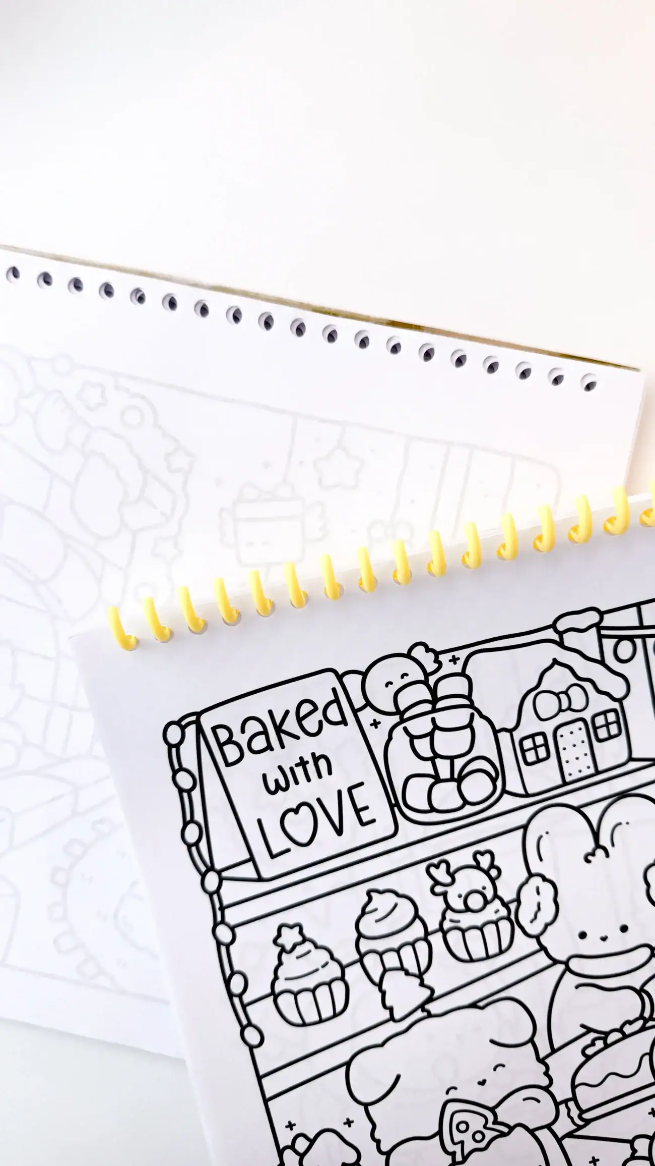 A yellow spiral coil being threaded through punched holes in a coloring book cover and interior pages.