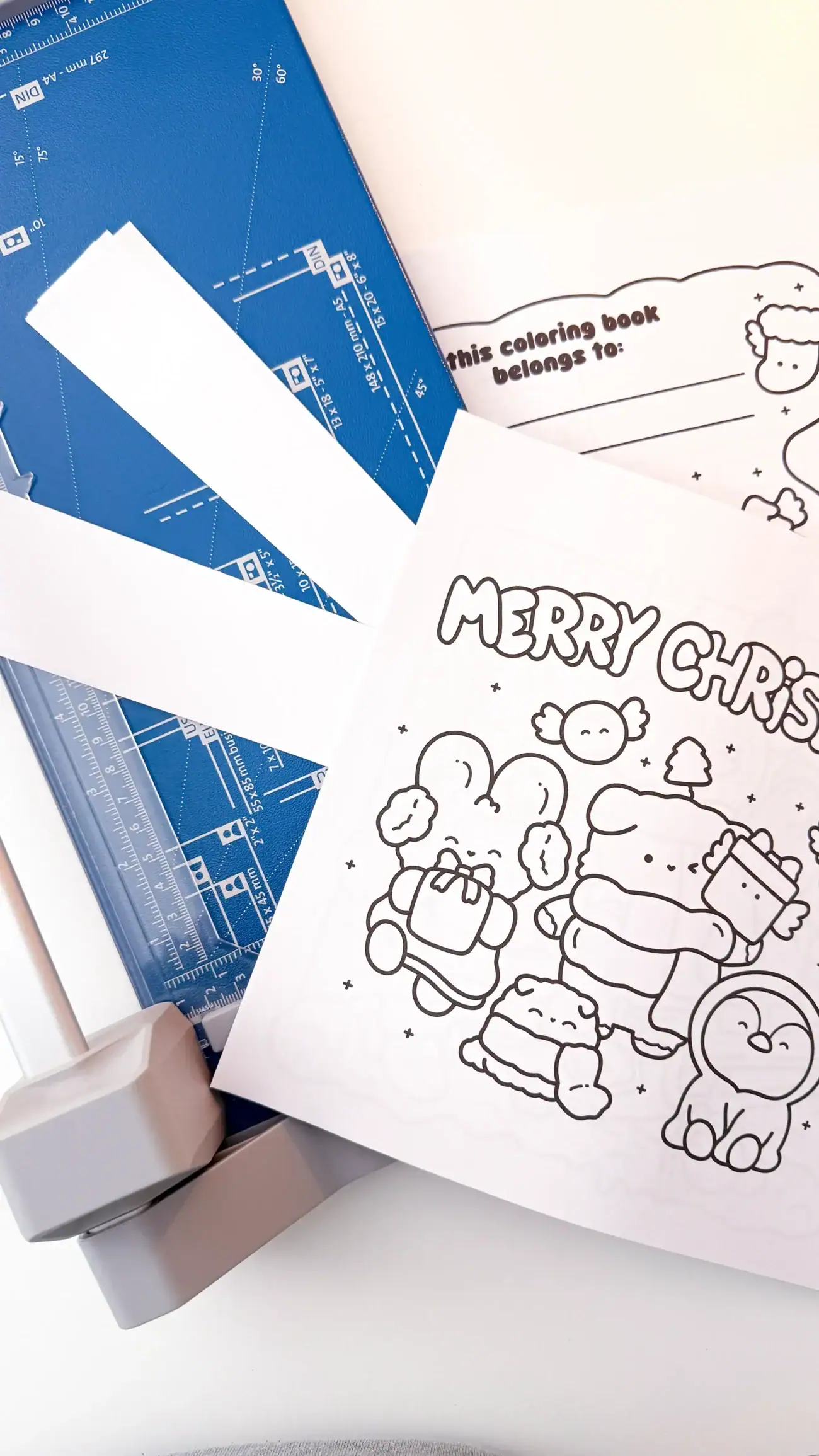 Printed coloring book pages and covers being trimmed to size using a blue paper cutter.