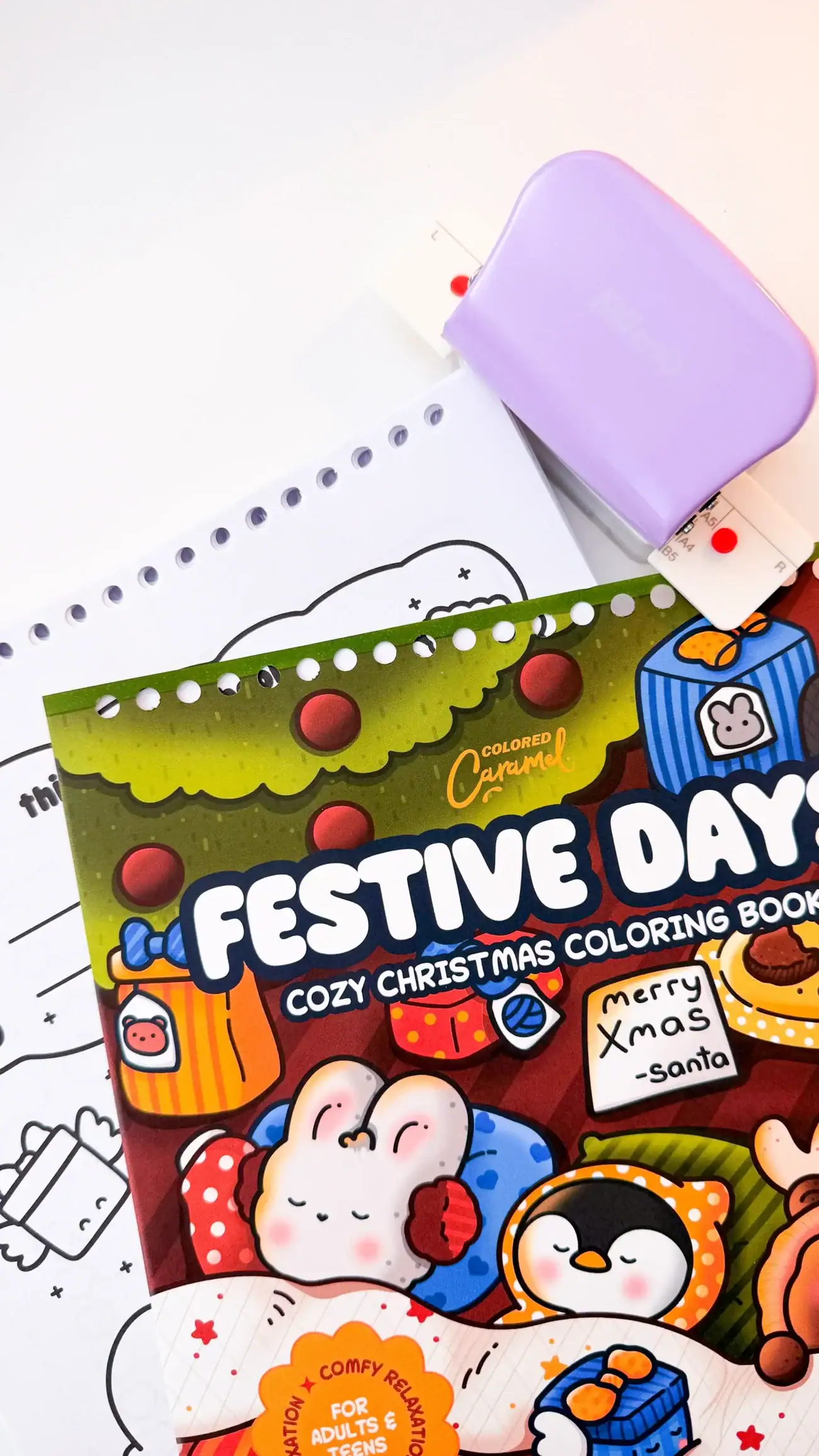 A purple 6-hole puncher creating evenly spaced binding holes along the edge of a coloring book cover and pages.