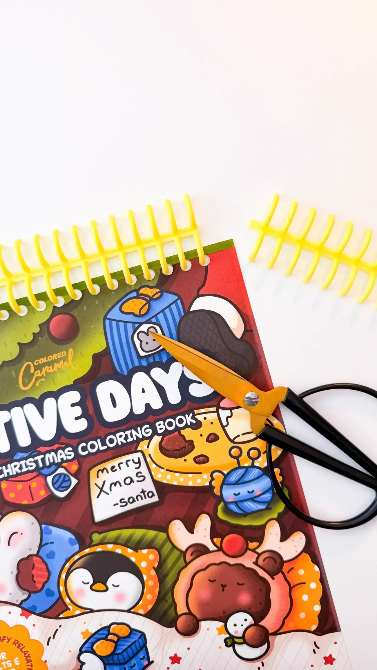 Scissors trimming a yellow spiral coil to fit the height of a coloring book before binding.