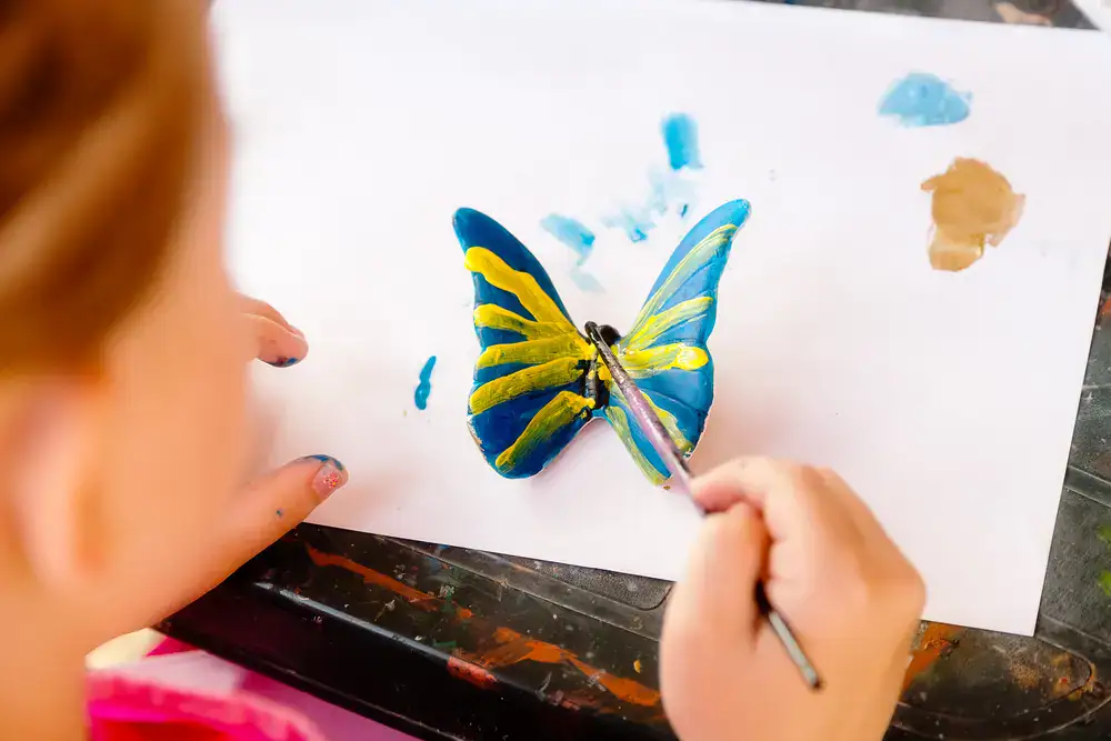 Künstlerin malt eine Schmetterlingsillustration, während sie Aquarellfarbe auf Papier aufträgt.