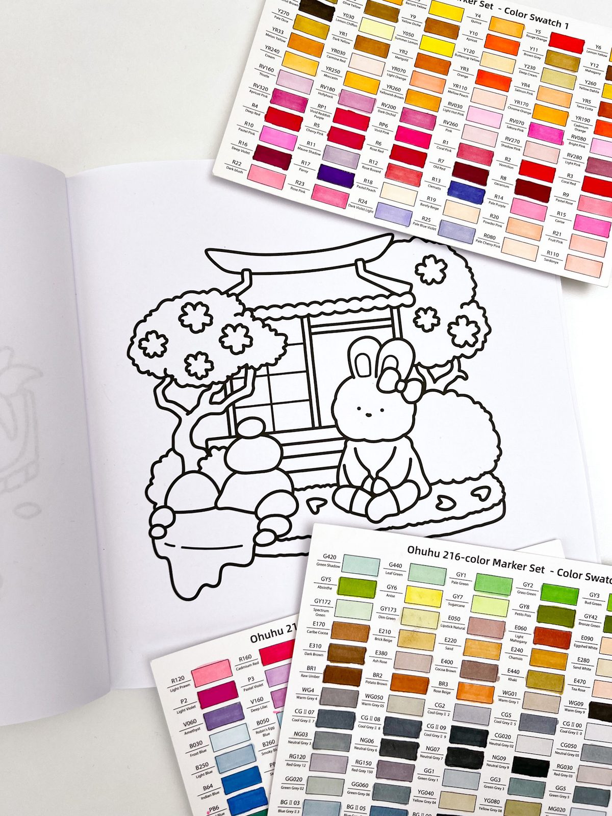 Open adult coloring book showing zen garden bunny illustration with marker swatch cards