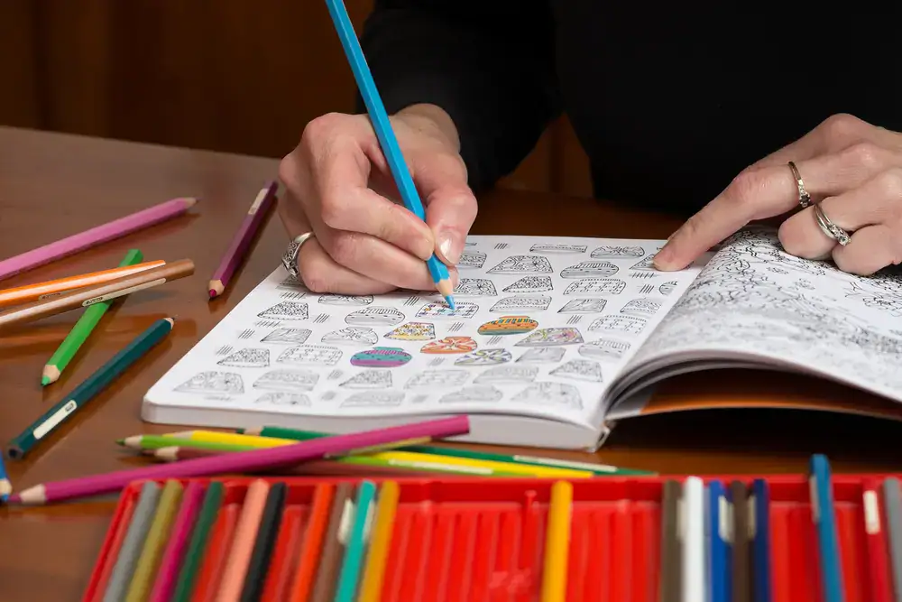 Hands coloring an adult coloring book page with a blue colored pencil