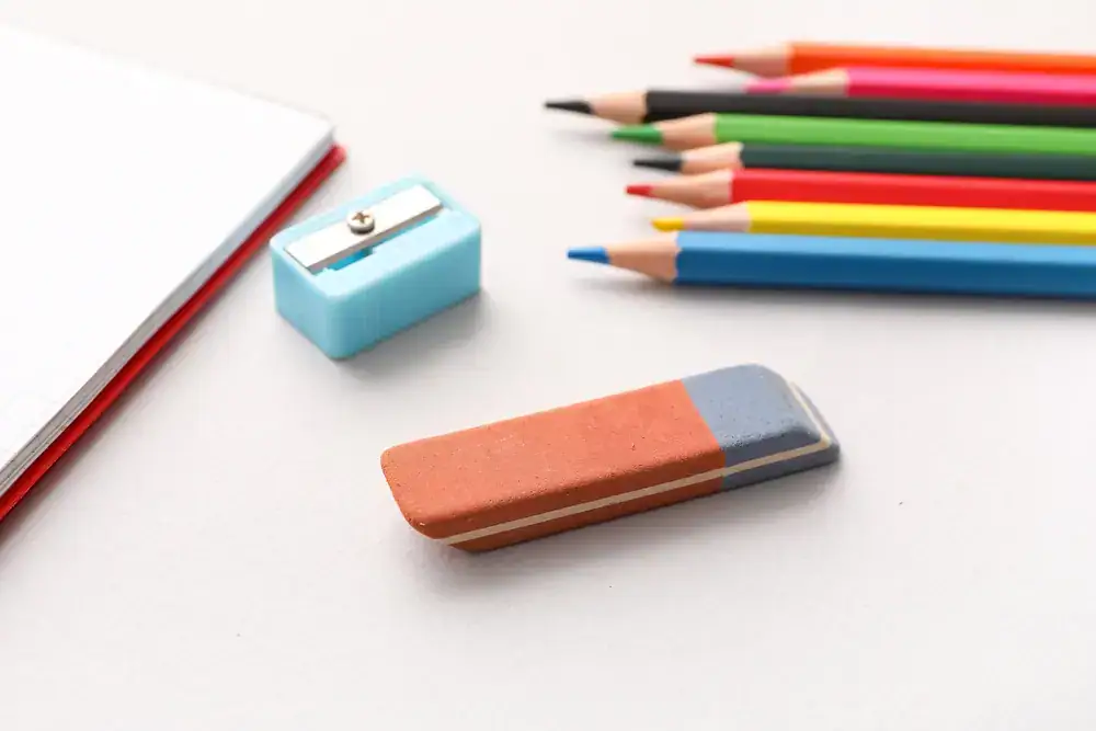 Colored pencils, a sharpener, and an eraser laid out on a white surface